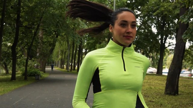 Attractive sexy runner brunnete woman with good shapes in green blouse running in park. Portrait super slow motion shot front. Hair flutter on wind.