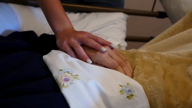 Young caretaker comforting a bedridden elderly man