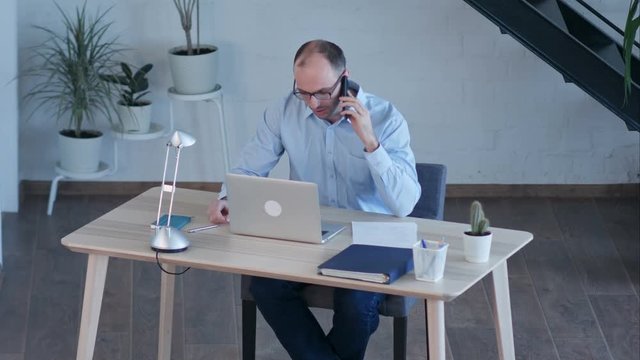 Businessman work on computer while talking on smart phone
