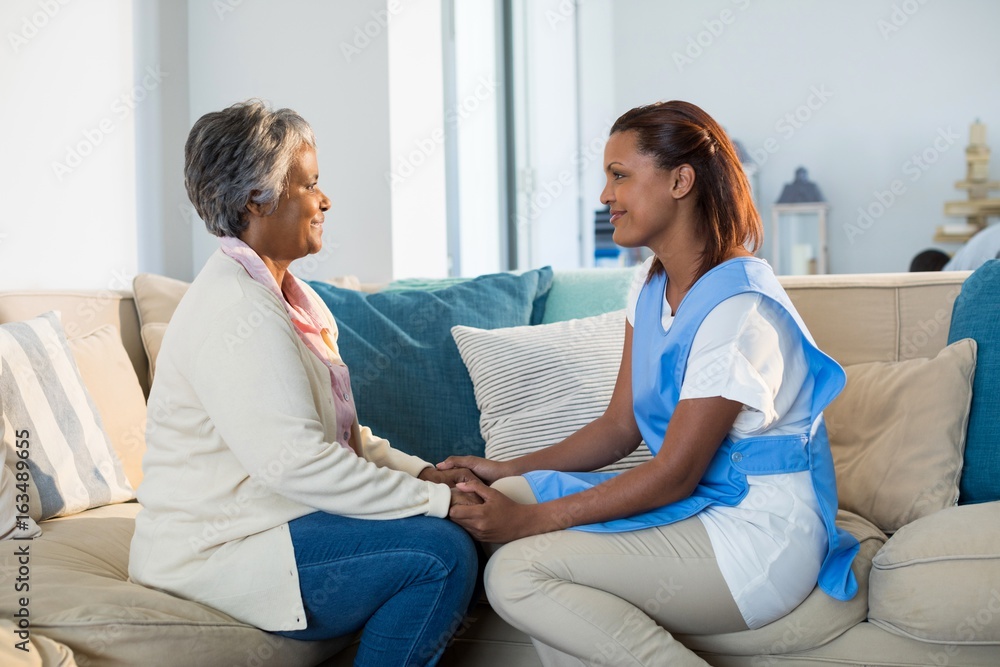 Wall mural Female doctor comforting senior woman in living room