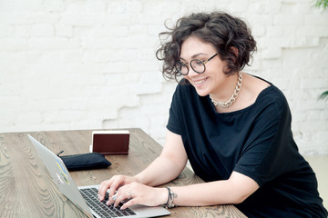 Young plus size female model sitting in front of the table, smiling and working on her notebook....
