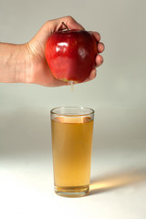 A woman's hand squeezes fresh juice. Pure apple juice pouring out from fruit into glass.