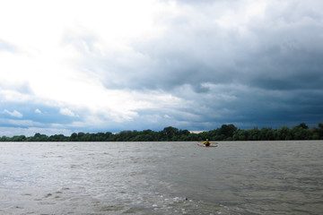 Man in selfmade wooden kayak in Danube river against background of storm sky. Kayaking in nature...