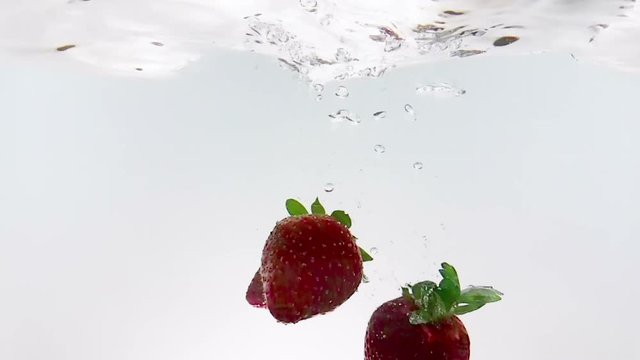 red fresh fruit strawberries falling into water with splash, shot in slow motion on white background, strawberry for health and diet, nutrition concept