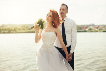 Fototapeta na wymiar Elegant gentle stylish groom and bride near river or lake. Wedding couple in love