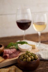 Green olives in container with ingredients and wineglasses