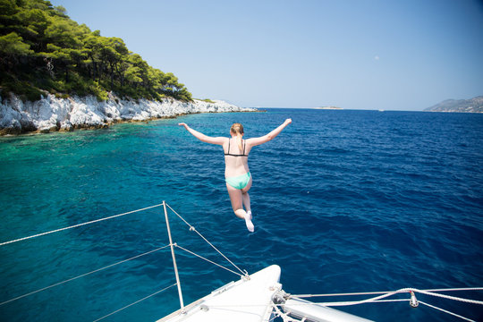 Girl jumping in clear Mediterranean water from a sailboat