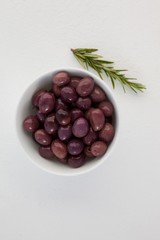 Overhead view of brown olives in bowl by herb