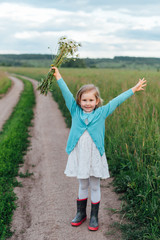 Child on the path with a bouquet of chamomiles in boots