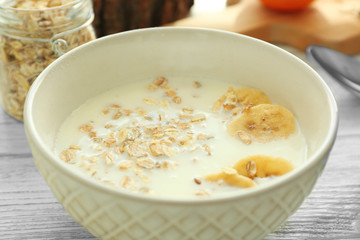 Bowl with oatmeal, milk and banana slices for breakfast on wooden table