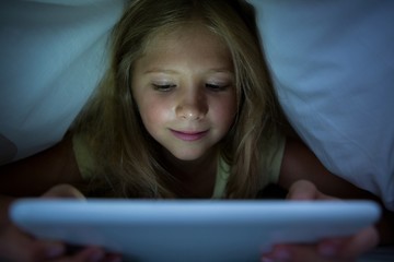 Girl using tablet computer under blanket