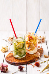 Two mugs of infused detox diet refreshing waters - first with cucumber and lemon, second with lemon and peach