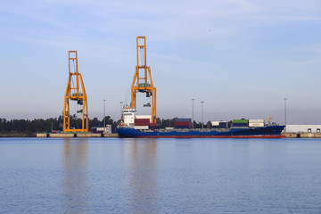 Obraz premium Cargo ship loading. Logistics and transportation with working crane bridge in harbor, logistic import export background and transport industry, Freight Transportation, Shipping, Nautical Vessel