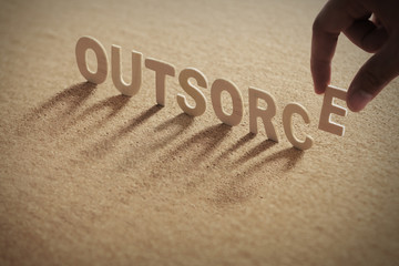 OUTSORCE wood word on compressed or corkboard with human's finger at E letter.