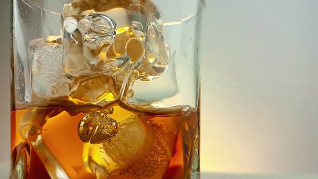 close-up of  barman pouring whiskey in the drinking glass with ice cubes on warm white background, time of relax drink with whisky, shot in slow motion