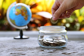 World globe map and money bank on table closeup garden leaf blur background. Concept of financial money saving