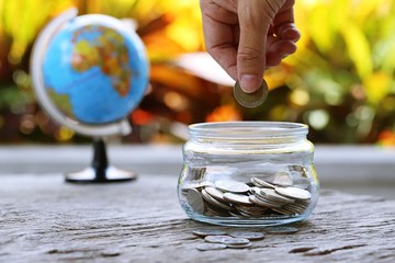 World globe map and money bank on table closeup garden leaf blur background. Concept of financial money saving