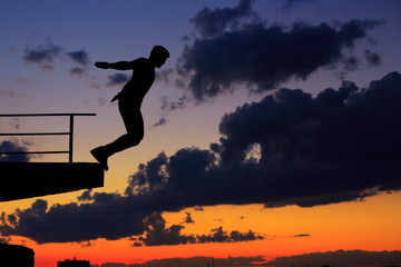 Man is jumping from edge of roof. Clouds and sunset
