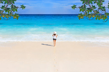Fototapeta na wymiar The girl walking on a white sand beach is a bright day. With blue sea and blue sky