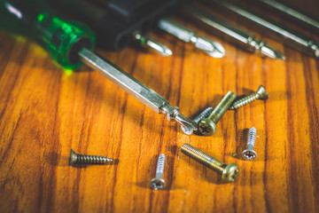 Close-up of screwdriver and small screw on tip set head screw driver and screw on wood background