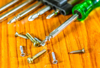 Close-up of screwdriver and small screw on tip set head screw driver and screw on wood background