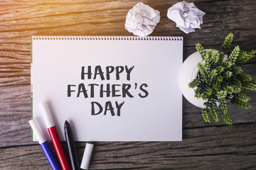 HAPPY FATHERS DAY word with Notepad and green plant on wooden background.