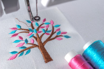 Marco close up image of embroidery cartoon tree design on workspace of machine and two threads cyan...