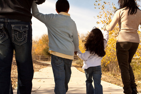 Rear View Of A Family Holding Hands And Walking.