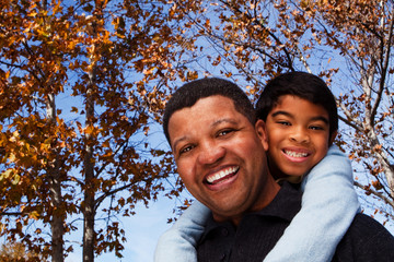 Biracial father and son laughing and smiling outside.
