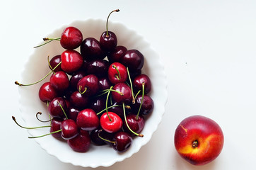 Красная вишня с зеленой веточкой на белой тарелке