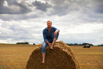Naklejka na ściany i meble man in jeans on hay on field.