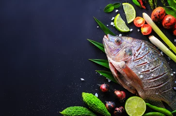 Photo sur Plexiglas Poisson Vue de dessus de délicieux poissons frais et herbes et épices, citron, tomate, piment et divers légumes sur fond de bois sombre, espace pour la texture. Alimentation saine, régime alimentaire ou concept de cuisine.
