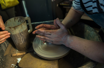 Hands working on a spinning pottery wheel, making pottery out of clay mud. close up photograph with a shallow depth of field.