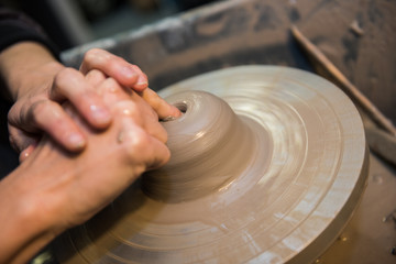 Hands working on a spinning pottery wheel, making pottery out of clay mud. close up photograph with a shallow depth of field.