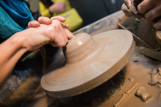 Hands working on a spinning pottery wheel, making pottery out of clay mud. close up photograph with a shallow depth of field.