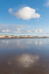 Fototapeta premium Beautiful blue sky and textured sand, on a cool sunny winters day at the beach. The clouds reflect off the wet sand.