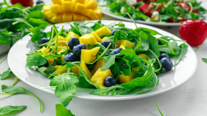 Mango, blueberries salad with arugula on white plate