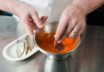 Organic Mackerel fish fillets, being marinated in a metal bowl of vibrant orange tandoori curry spices and sauce, being prepared for further cooking .