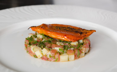 Organic tandoori Mackerel fish fillets, marinated in a vibrant orange tandoori curry sauce, prepared on a white plate with potato, pomegranate and lime wedges.