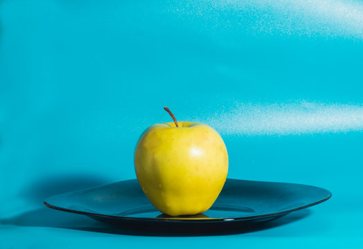 yellow Apple in the plate on a blue background.