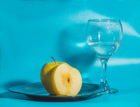 yellow Apple in the plate with a glass of water on a blue background.