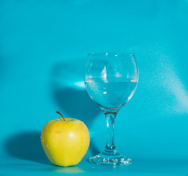 yellow Apple with a glass of water on a blue background.