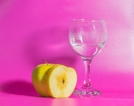 yellow Apple with a glass of water on a pink background.