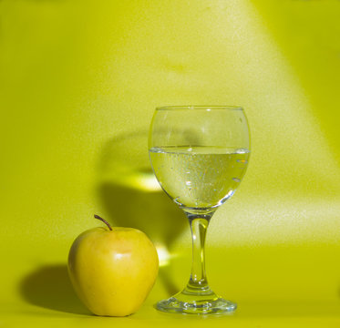 a glass of water and a yellow Apple on a green background.