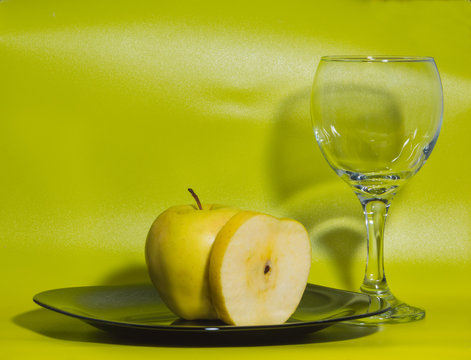 a glass of water and yellow Apple on plate on green background.