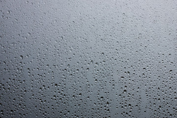 Rain drops on glass against the grey rainy sky