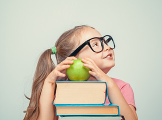 beautiful cute little girl with books and green apple smiling and looking up