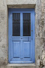 Old and worn blue wooden door with glass and ironwork in Les Baux, France
