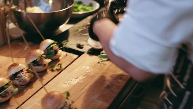 Close focus on process of making small tiny burgers with smoked pork meat in small outdoor kitchen with catering for private party. Handheld shot