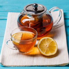 Glass cup of tea with lemon and glass teapot.